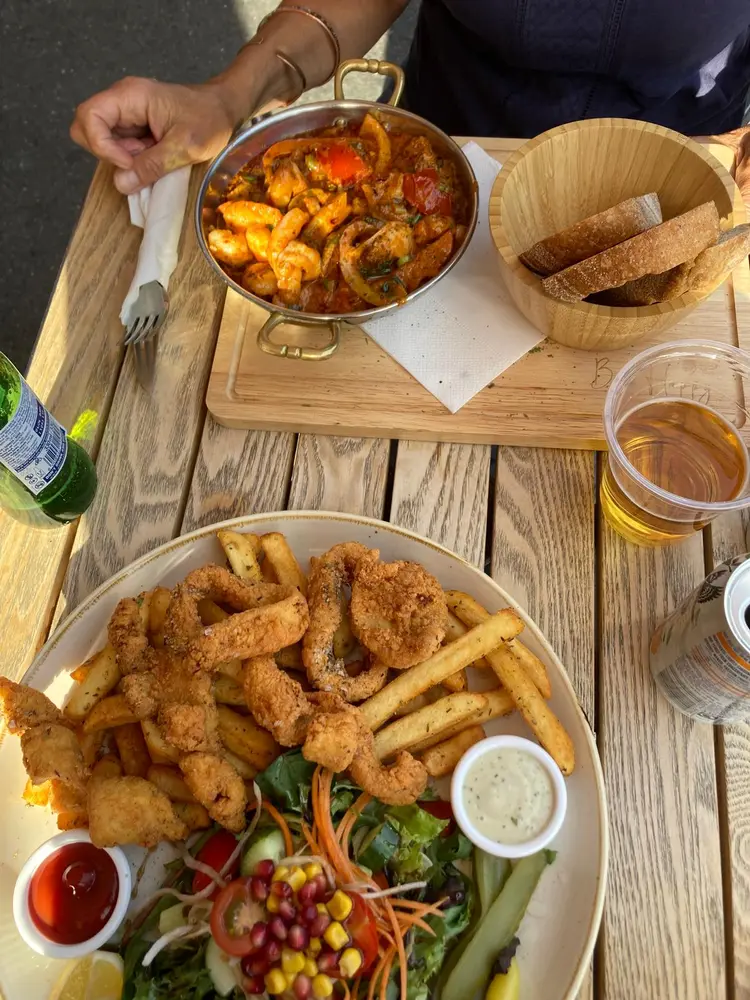 Plate of fried calamari with chips, salad and dips beside a pan of prawns in tomato sauce on a wooden canalside table
