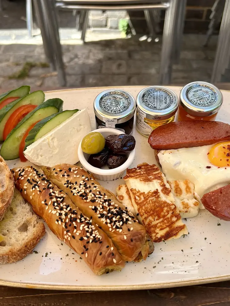 Turkish breakfast plate with feta, olives, cucumber, tomato, grilled halloumi, sucuk, fried egg, sesame börek and toast